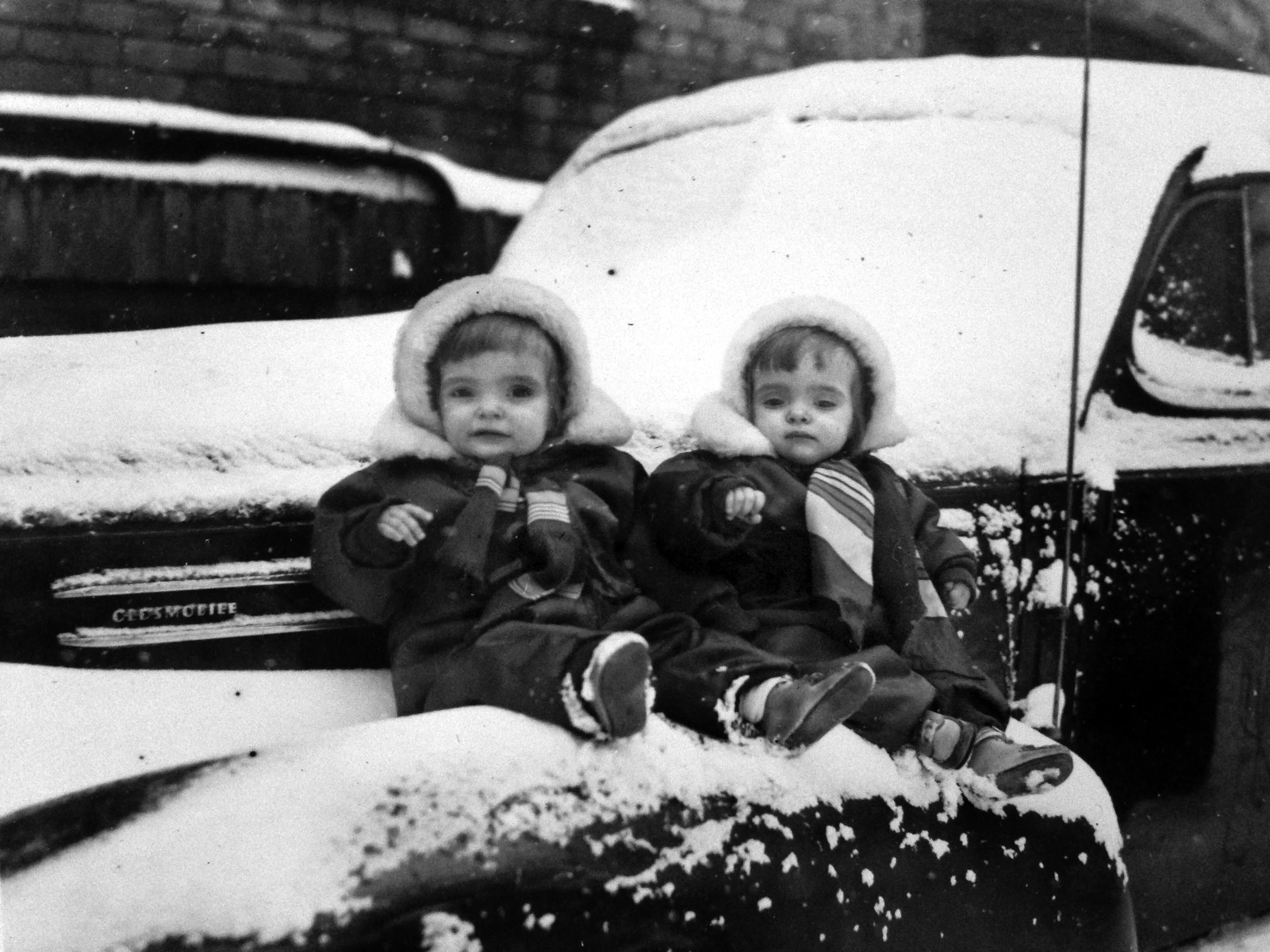 As 2-year-olds, twins Jane and Joan Schleiter wait for the 1949 Winter Carnival parade on a fender of the family Oldsmobile. (Courtesy of Jane Lonergan)