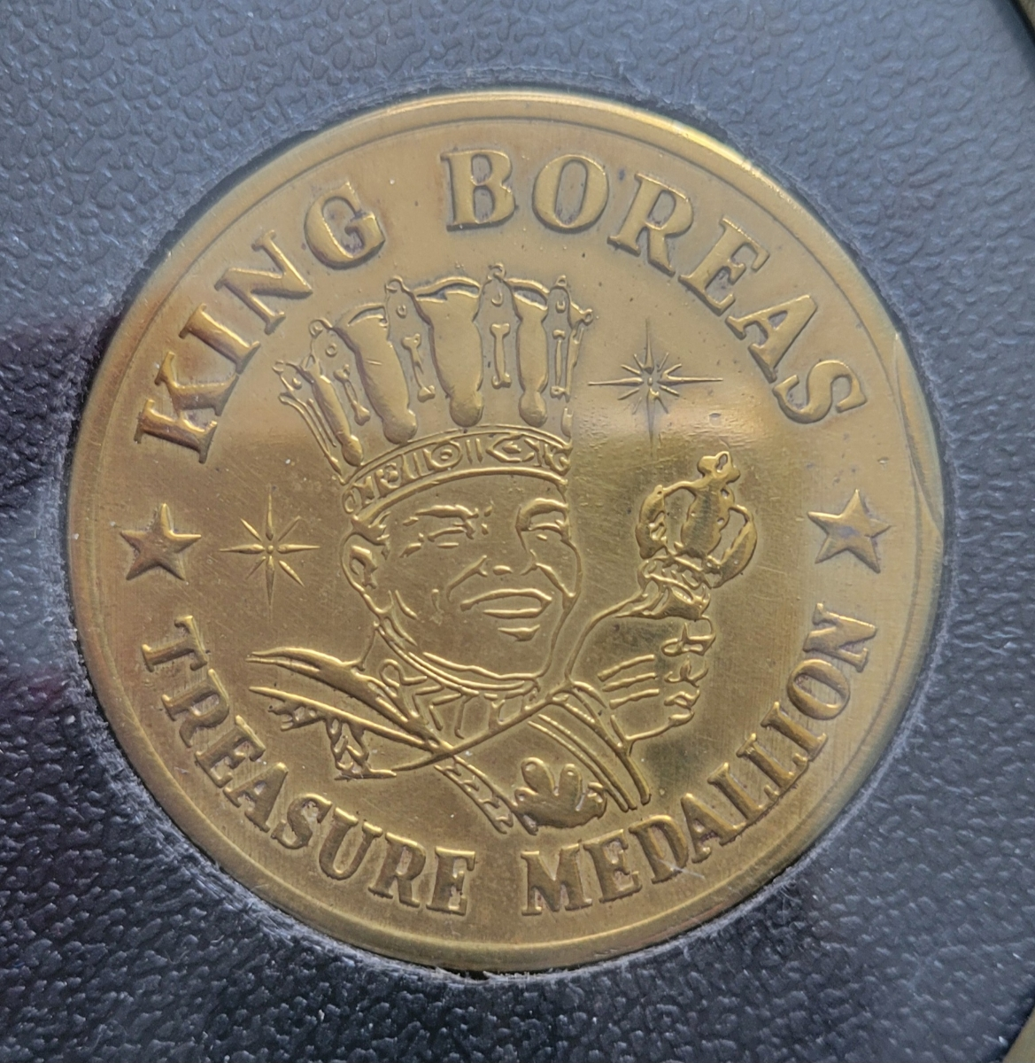 A gold medallion with an illustration of a king wearing a crown and holding a scepter. The writing on the coin reads King Boreas Treasure Medallion