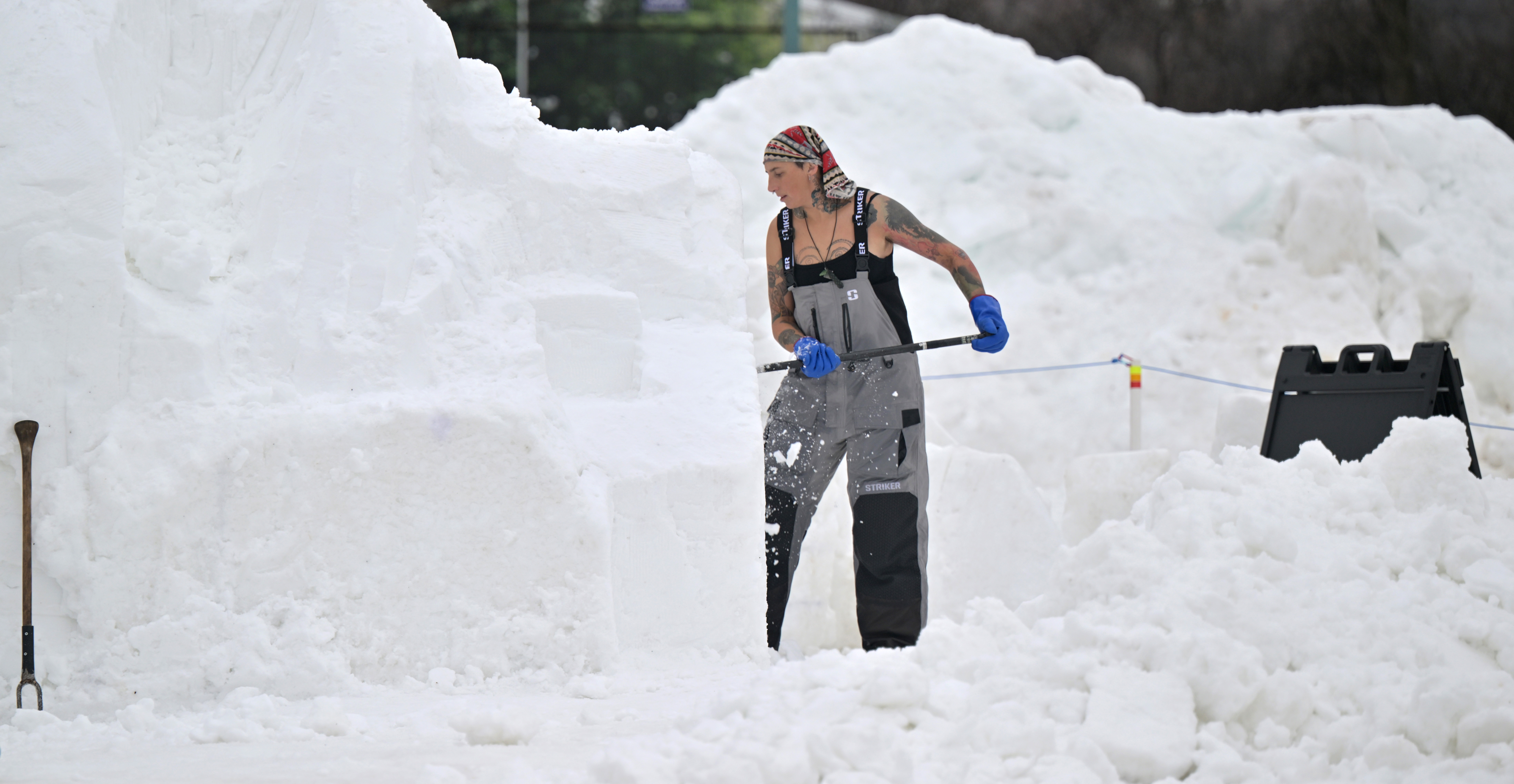 A person carves a block of snow in overalls and a tank top