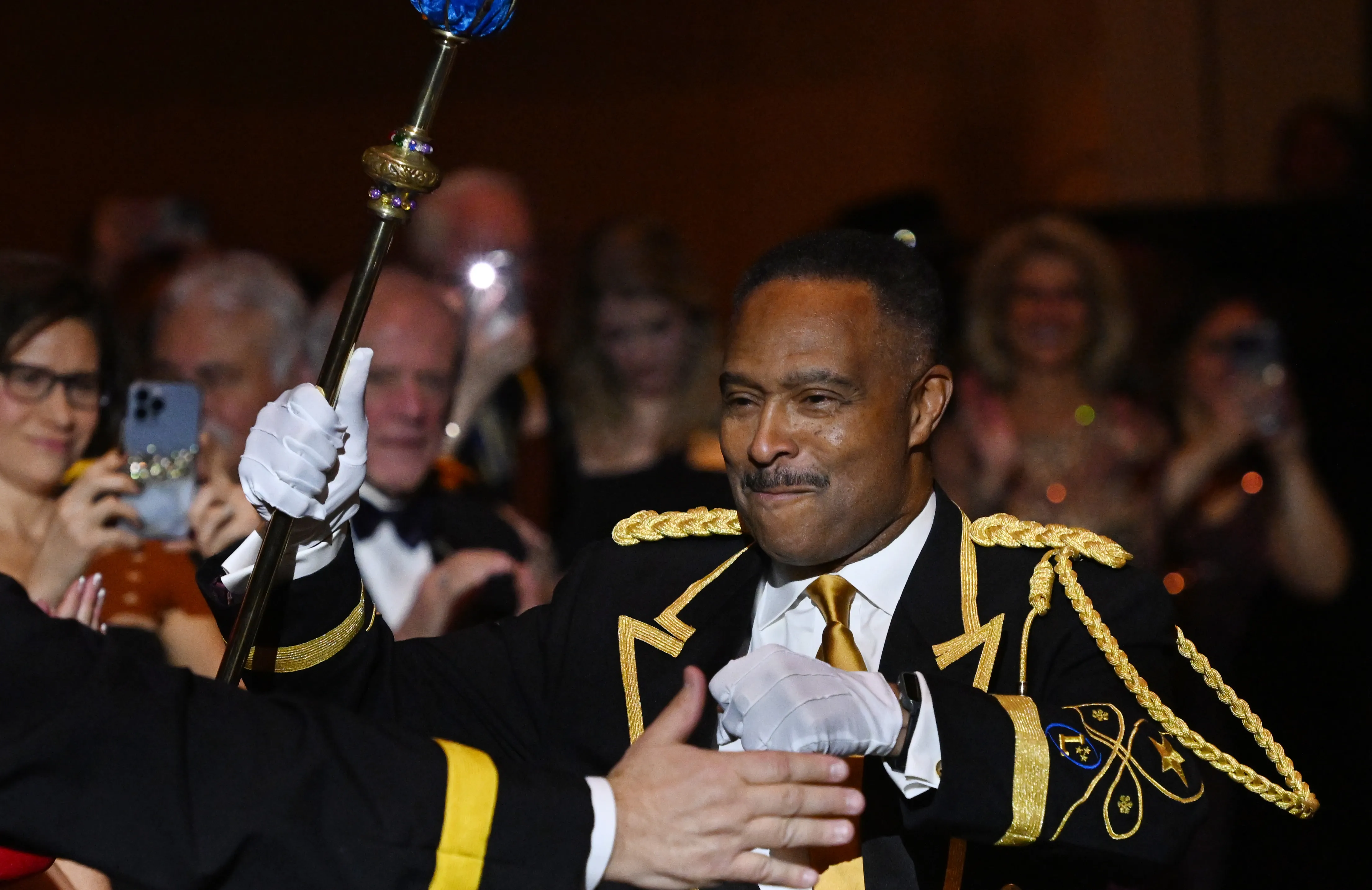 A man raises a scepter as others applaud him.