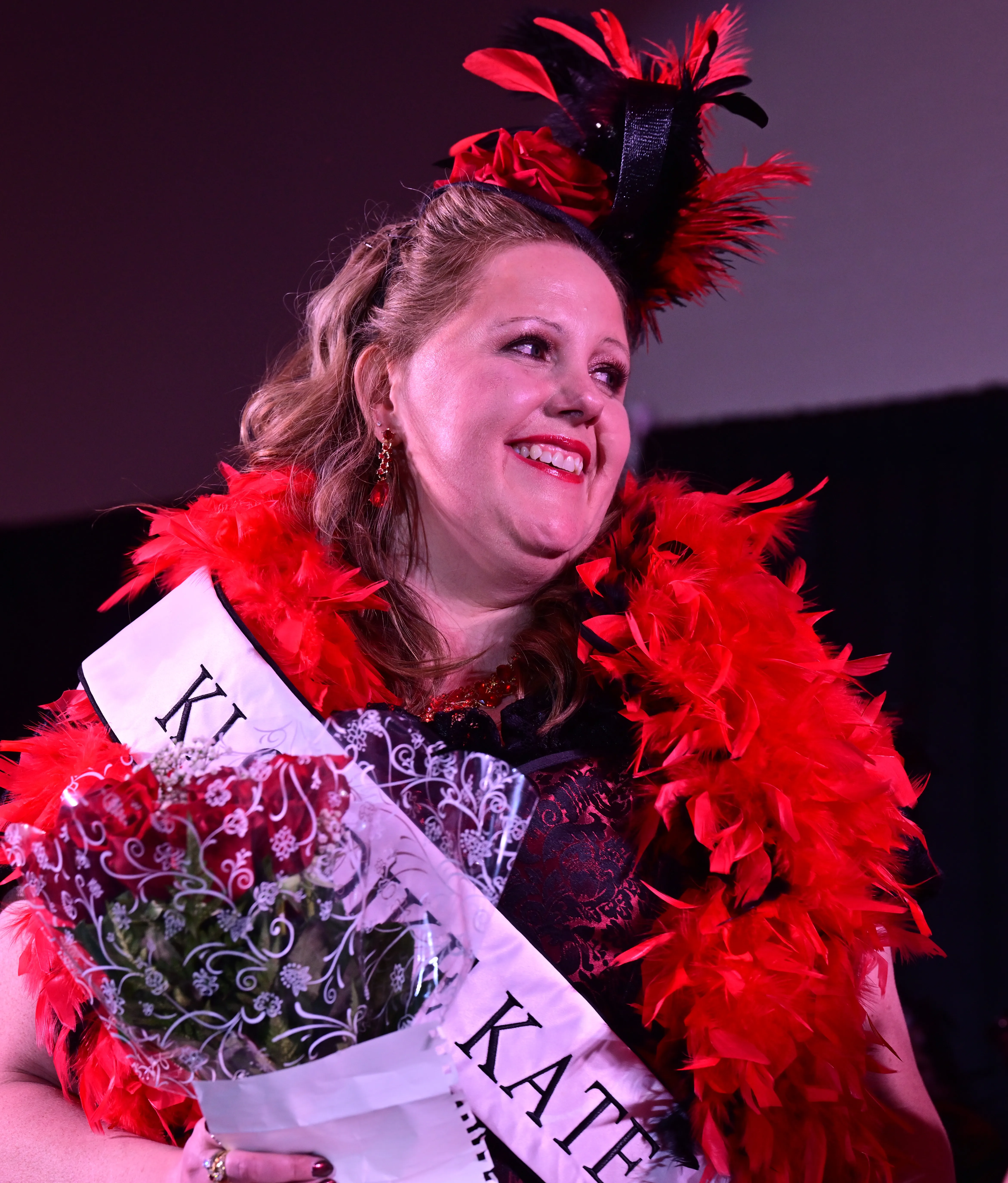 A woman in feather boa holds a bouquet and smiles.