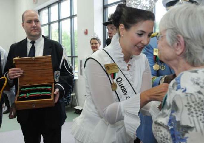 Mike Meents, a King's Guard for the 2010 Winter Carnival, left, holds a box which contains medals for Knighting awards, while his sister, Gretchen Spier, 2010 Queen of Snows honors Betty Magnuson, as she pins her medal on at Merrick, Inc, a nonprofit in Vadnais Heights that hires adults with developmental disabilities. Meents is being treated for Leukemia and has had to split his time in order to participate in a clinical cancer trial in Chicago. He attends every Carnival function he can when he's back home