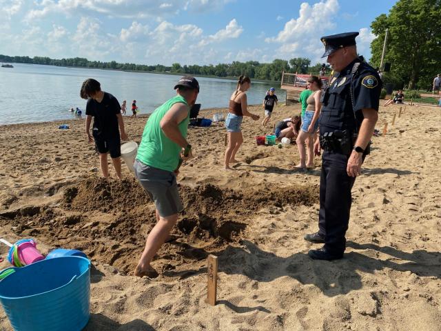 Litchfield Police officer Gary Gruenke inspects the work of Chris Woelfel during the sand sculpture contest Friday afternoon at Lake Ripley. Gruenke also served as the grand marshal for the parade.