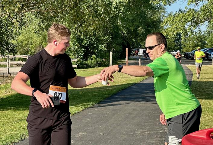 Levi Schmidt grabs a cup of water from race co-organizer Jim Watt at the hydration station on the west side of Lake Ripley.
