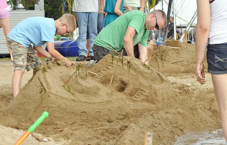 Luke Primus of Hutchinson, right, sculpts a sunken ship with son Mason, 12, during Watercade's sand sculpture contest Friday night at Lake Ripley's beach.