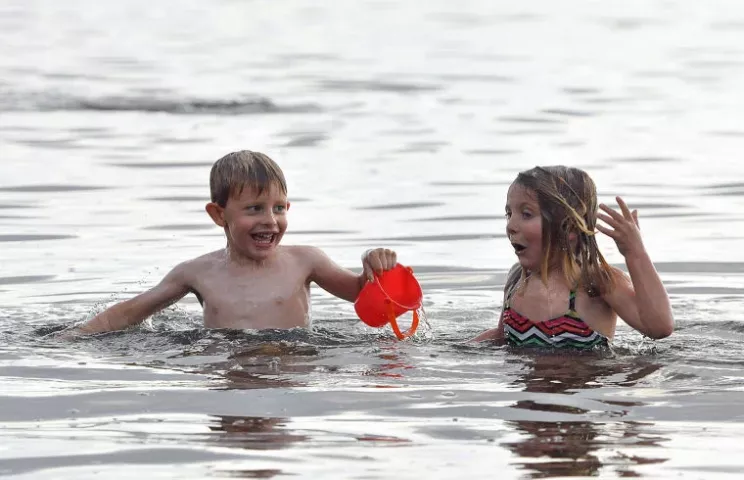 4-year-olds Griffin and Siena Prevost of Minneapolis take a dip in Lake Ripley's cool water Friday evening. The children helped their nanny, Sara Binsfeld of Litchfield, create a sand castle during the Watercade sand sculpture contest.