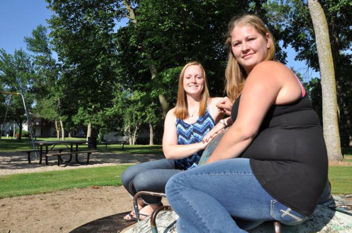 Alissa Holmgren, left, and Chrystal Swanson, both of Litchfield, sit on a merry-go-round, where they found the Watercade Medallion on Monday at Northside Park.