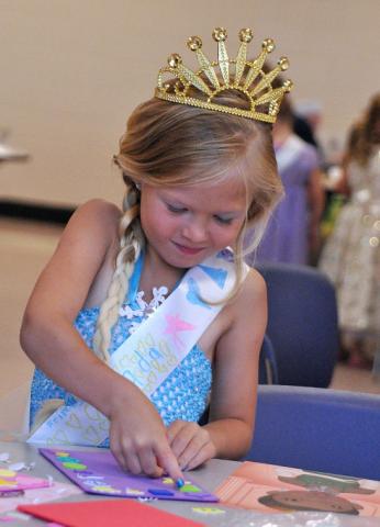 6-year-old Jada Rosenquist, dressed as Elsa from Disney's “Frozen,” places stickers on a princess-themed frame.