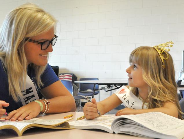 Five-year-old Natalie Ross smiles at Watercade queen candidate Maddie Maahs while coloring Monday night at the Prince and Princess for a Day event.