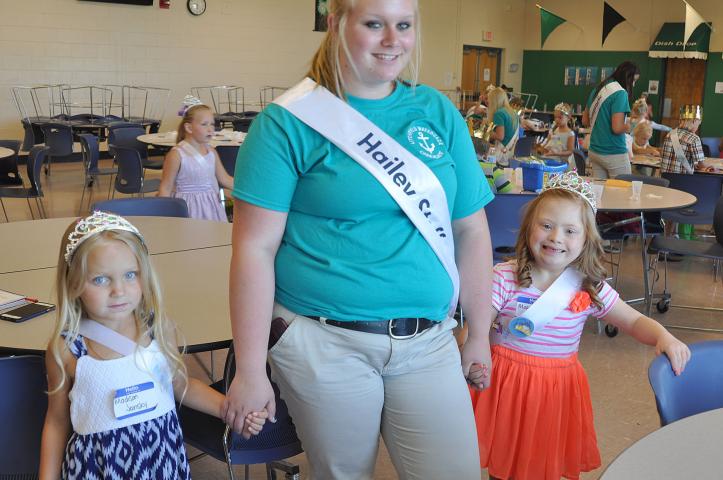 Madison Jansky, left, and Maggie Gaulrapp, right, hold Watercade candidate Hailey Stoffer’s hand as they wait to take their professional photo with the Watercade royalty.