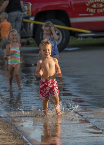 Lucy Kadelbach, 4, chases her brother Calvin, 4, as they play in the water from the water-ball fight Friday evening.