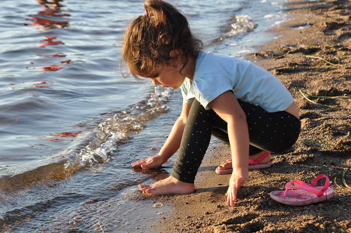 Eva Cervantes, 3, runs her hands through the tide at Friday night’s beach party at Lake Ripley Beach.