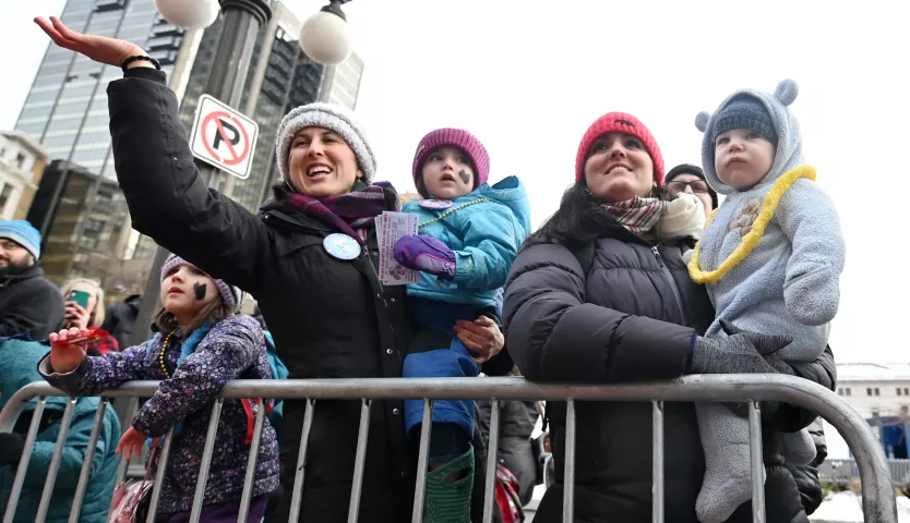 Katlyne Slate, waving, holds 2 year-old Raiya with her daughter Madeline, 4, on her right as he sister Lindsay Edwards, holding 10 month old Wally Nelson, watch the 2020 St. Paul Winter Carnival King Boreas Grand Day Parade in downtown St. Paul on Saturday, Jan. 25, 2020. (John Autey / Pioneer Press)